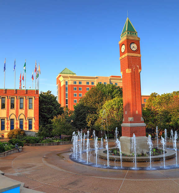 A large building with a clock tower and a fountain in front.