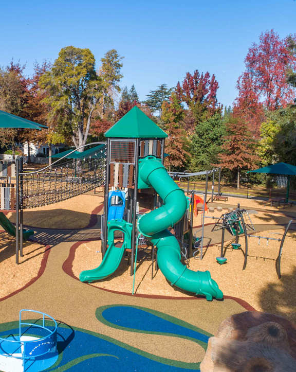 A playground with a blue slide and a green umbrella.