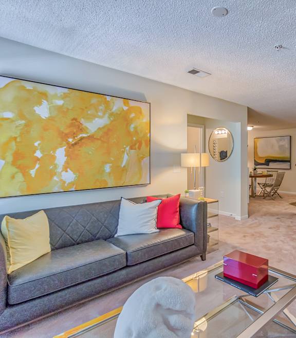 A living room with a grey couch and a yellow and orange painting on the wall.