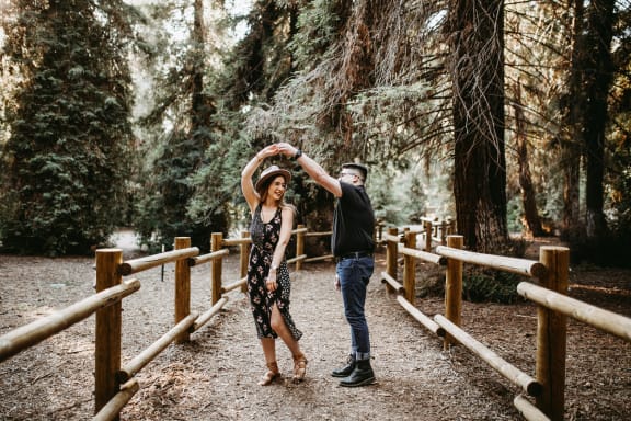 a man and woman dancing on a bridge in the woods