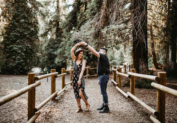 a man and woman dancing on a bridge in the woods