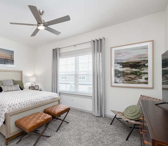 A bedroom with a large bed, a bench, and a ceiling fan.