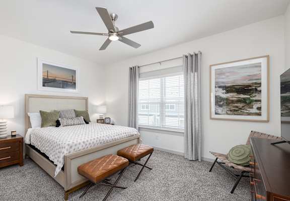 A bedroom with a large bed, a bench, and a ceiling fan.