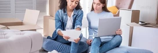 two women sitting on the floor looking at a laptop computer