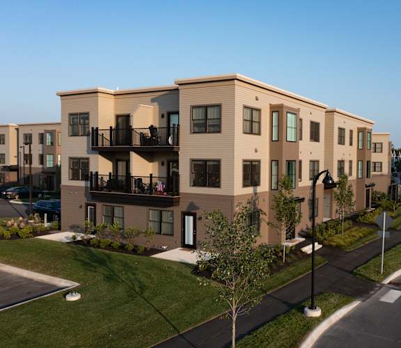 A row of modern townhouses with balconies and a street in front.