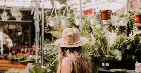 a woman in a straw hat standing in a greenhouse