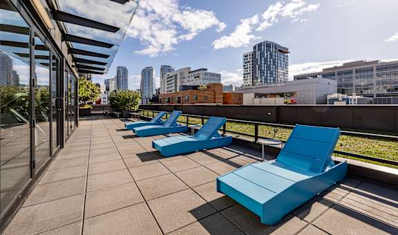 an outdoor deck with blue lounge chairs and a city skyline in the background