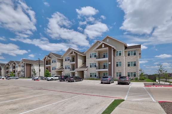 A large apartment complex with a parking lot in front.