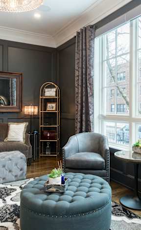 A living room with a grey couch, a grey armchair, a grey ottoman, and a black and white rug.