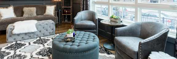 A living room with a grey couch, a grey armchair, a grey ottoman, and a black and white rug.
