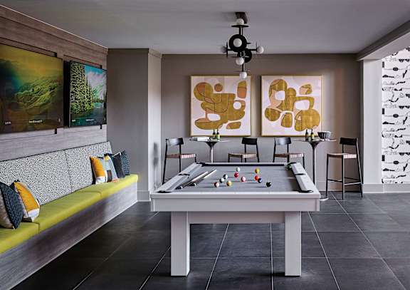 A billiard table is in the middle of a room with a green bench and two paintings on the wall.