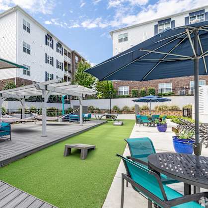 a patio with blue chairs and umbrellas and a green turf at The Met Apartment Homes, Hattiesburg, 39402
