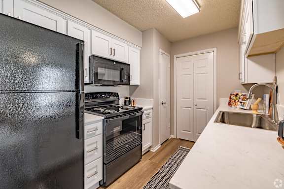 A black refrigerator is in a kitchen with white cabinets. at Highland Park, Texas, 76132