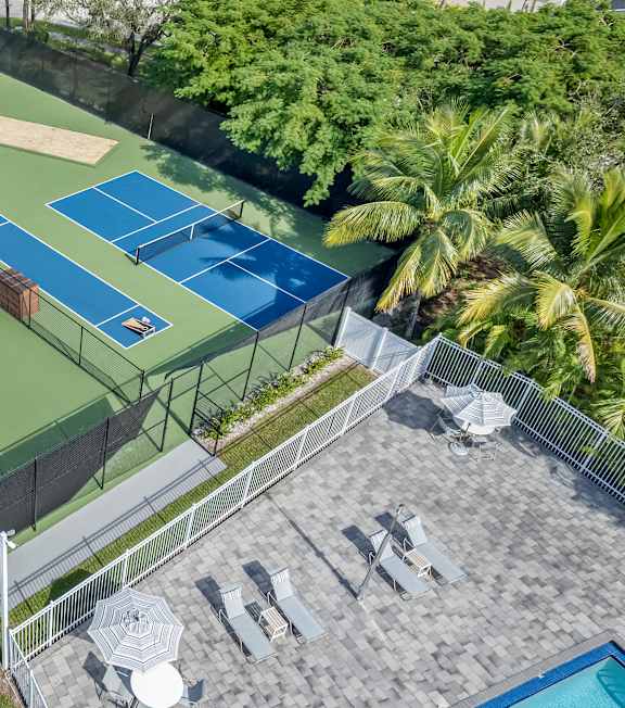 A tennis court with a blue surface and white lines is surrounded by a fence and trees.