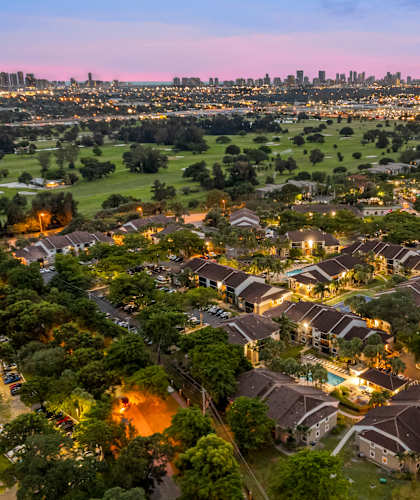 an aerial view of a neighborhood at dusk with the city skyline in the background