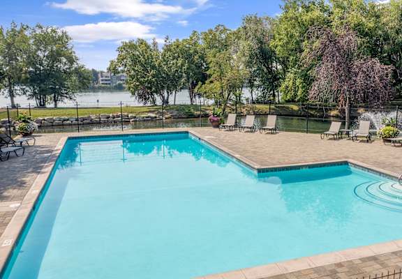 a swimming pool with chairs and trees and a lake in the background at Edgewater Apartments Boise, Boise, 83703