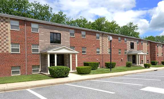 A row of red brick apartment buildings with green trees in the background. at Liberty Gardens Apartments, Baltimore, Maryland
