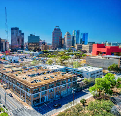 A cityscape with a mix of modern and older buildings, a clear blue sky, and a road with cars.