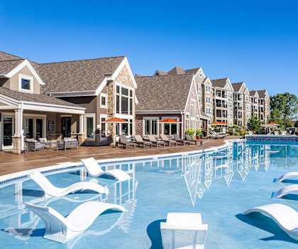 a large swimming pool with white chairs in front of apartment buildings