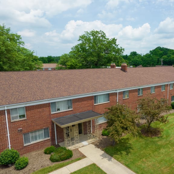 an aerial view of a brick building with a lawn and trees