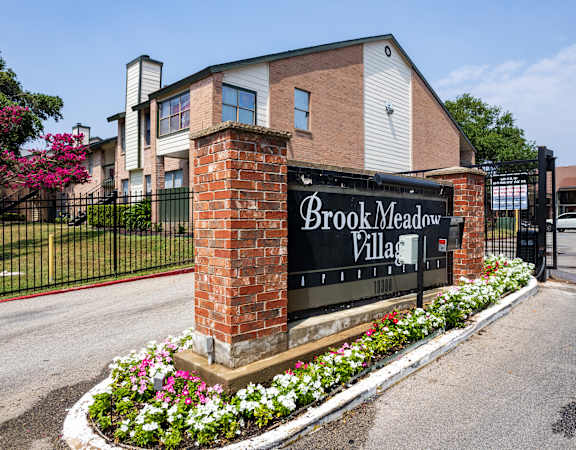 A sign that says Brook Meadow Village is in front of a building.