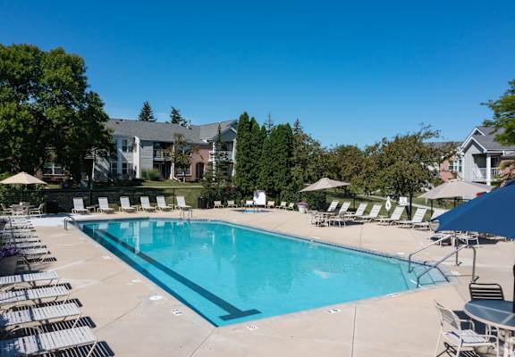 a swimming pool with chairs and umbrellas and apartments in the background