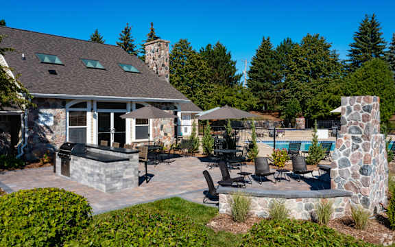 A house with a stone chimney and a patio with chairs and a table.