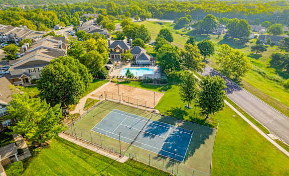 A tennis court is surrounded by a green lawn and trees.