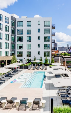 an outdoor pool with lounge chairs and umbrellas in front of a building