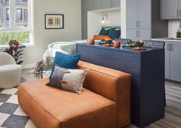 a living room with a brown couch and a kitchen with a blue counter