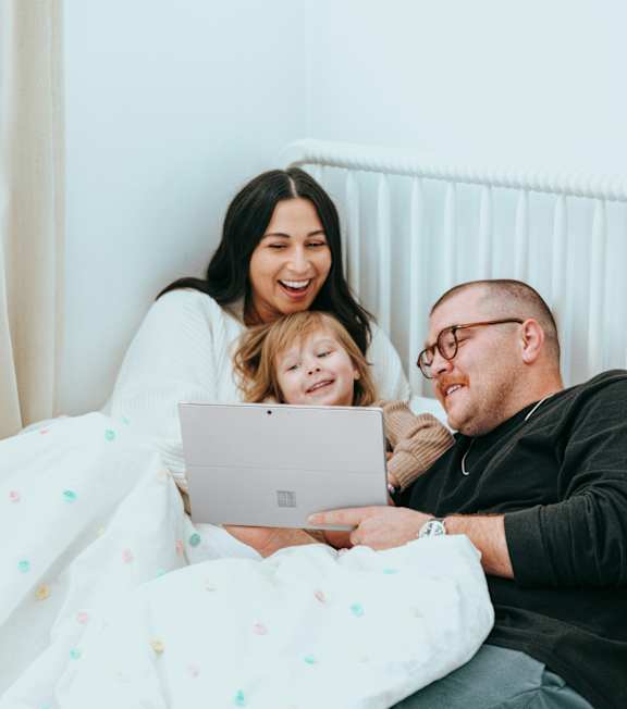 A family is sitting on a bed with a laptop.