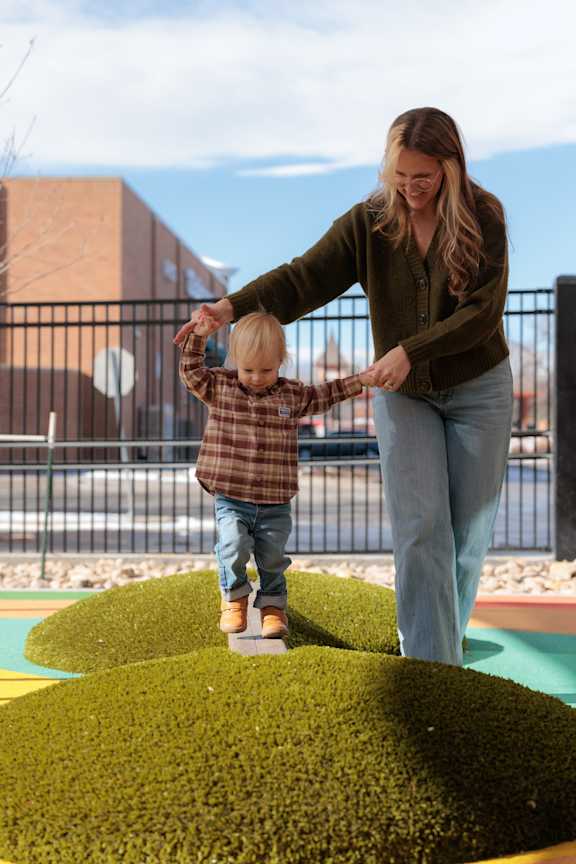 A woman and a child are playing on a green artificial grass surface.