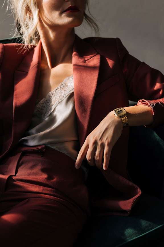 A woman in a red suit is sitting with her hand on her thigh.