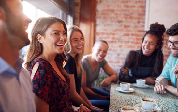 A group of people are gathered around a wooden table, enjoying a pizza and beer together.