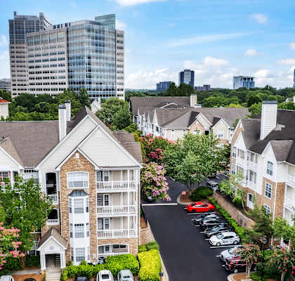 A view of a residential area with apartment buildings, cars parked in a lot, and trees.