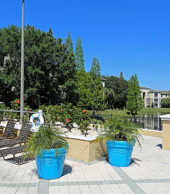 a patio with chairs and potted plants near a pond