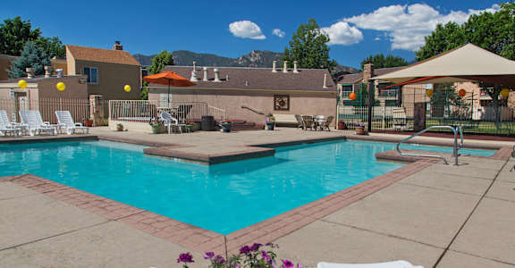 A pool surrounded by white chairs and a patio umbrella.