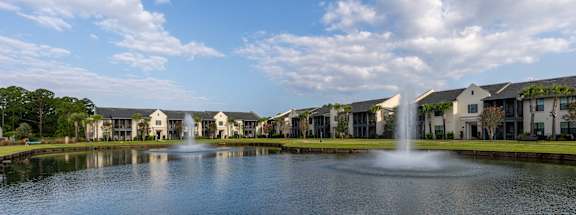 A fountain in the middle of a lake in front of apartment buildings.