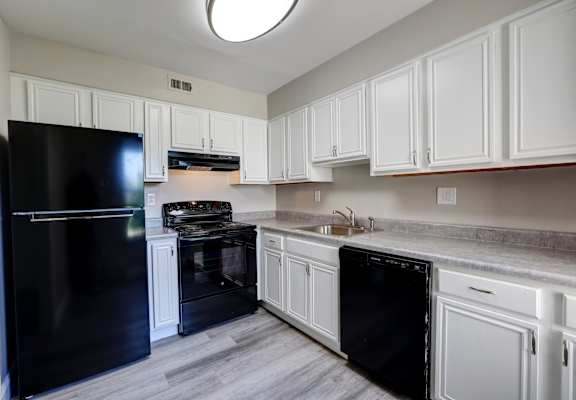 A black refrigerator is in a kitchen with white cabinets.