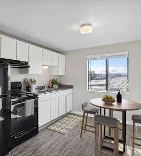 A black fridge and oven in a white kitchen with a table and chairs.