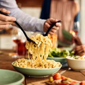 A person is serving spaghetti from a bowl into a plate.