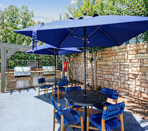A blue umbrella shades a table and chairs outside.