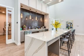a kitchen with a large white island with a long countertop and a row of black chairs