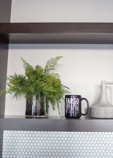 A shelf with a plant, two cups and a bottle on it.