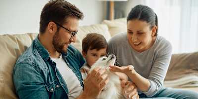 A family of three is sitting on a beige couch with a white cat.