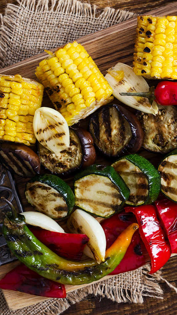 skewers of grilled vegetables and corn on a cutting board