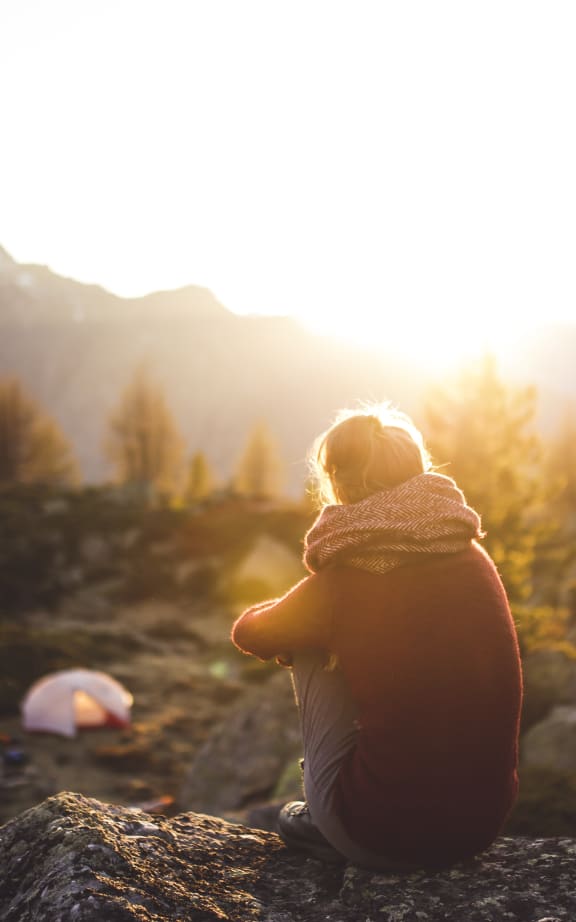 a woman sitting on a rock watching the sunset in the mountains