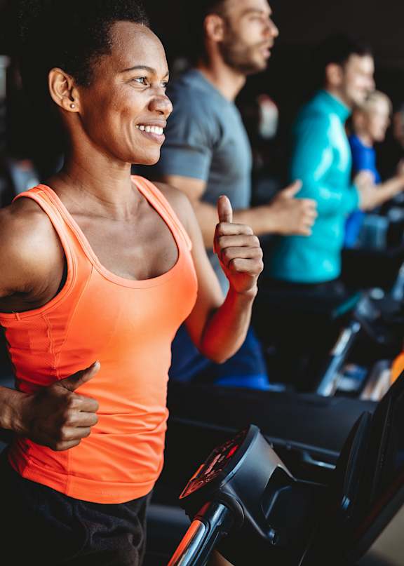 A man in a white t-shirt is running on a treadmill in a gym with other people exercising around him.