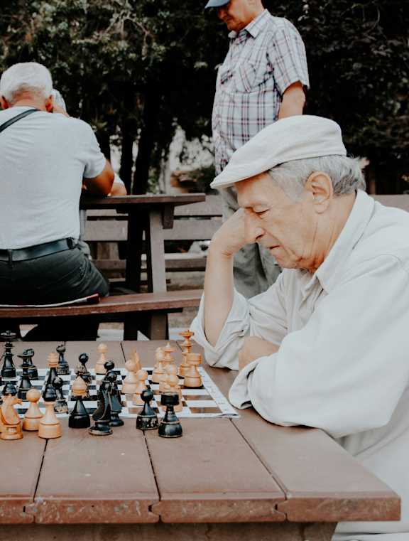 A group of elderly men playing chess outdoors.