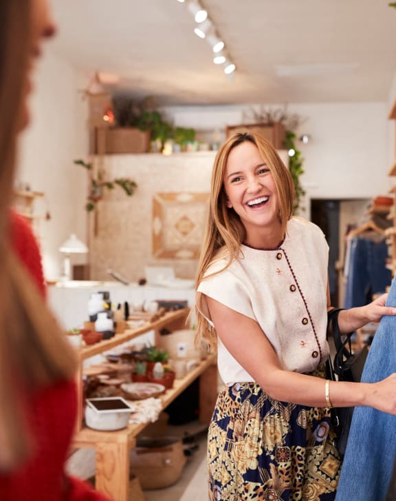 a woman smiling while looking at clothes on a rack in a clothing store